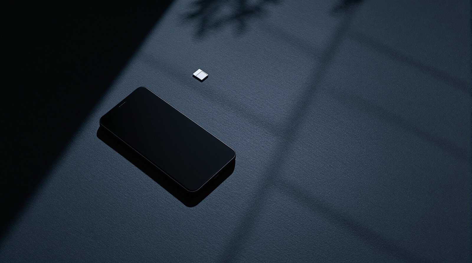 A small phone lying on a dark surface beside a SIM card and a tray tool